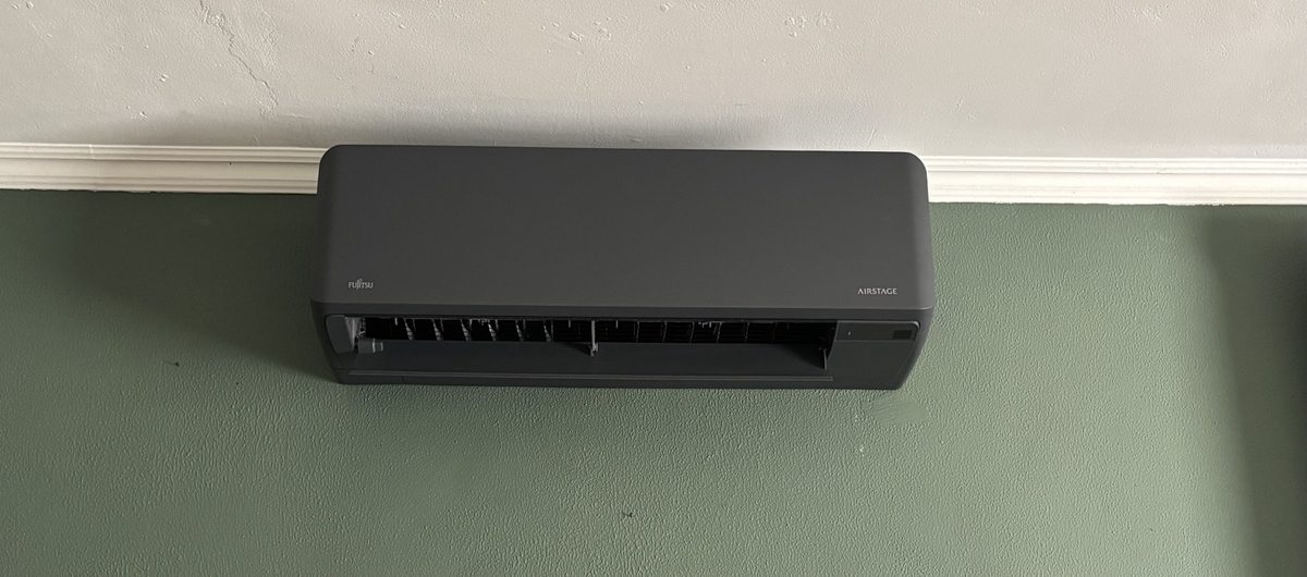 Antracietkleurig Fujitsu Airstage wandmodel tegen een groene wand